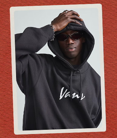 A young man wearing a black Scripted Vans Pullover Hoodie and sunglasses on a red holiday background.