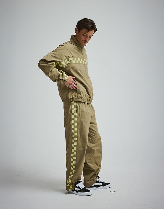 A young man puts his hand in the pockets of the bayleaf green Ronnie Track Jacket in a photography studio.