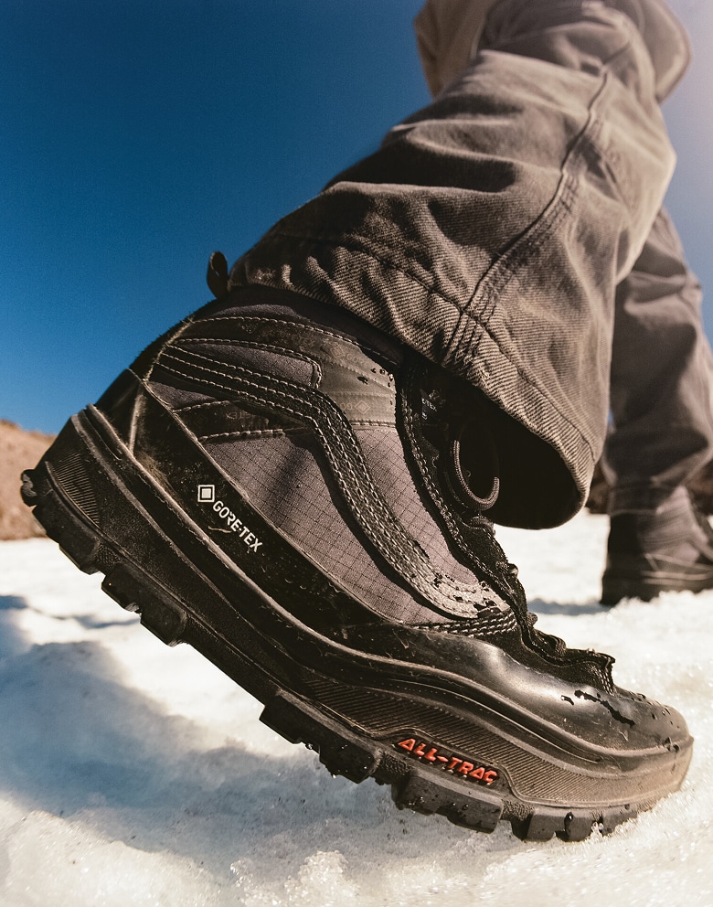 Person wearing a pair of the Sk8-Hi GORE-TEX Insulated Shoe in Black stepping on snow with blue sky in the background.