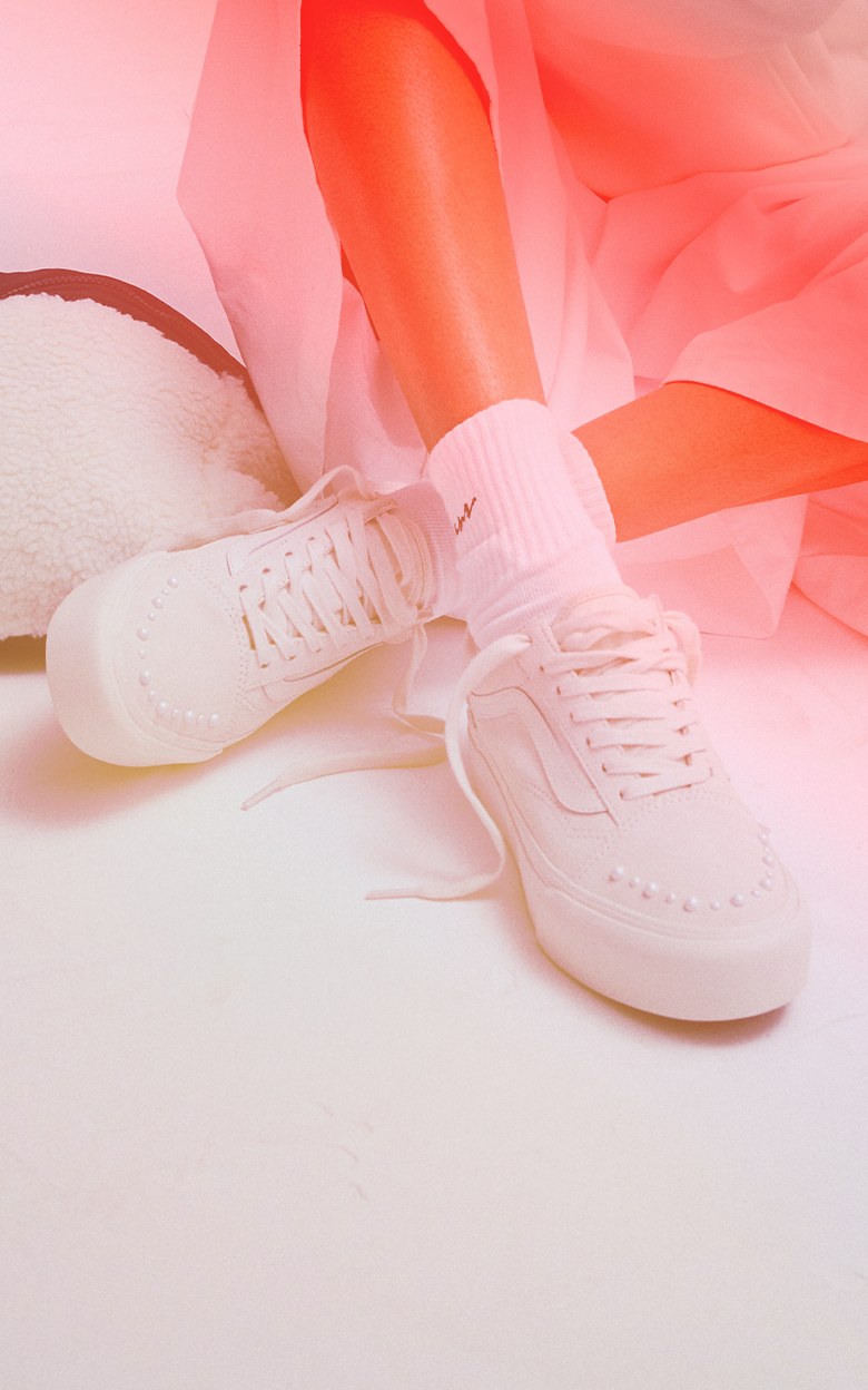 Close up of a person sitting down wearing a pair of Old Skool Platform Shoe in Pearlized Marshmallow White with an orange and red gradient covering them.