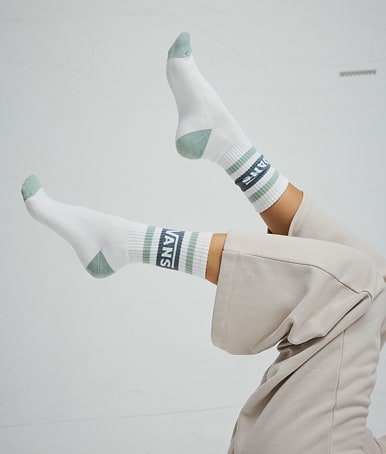 Person kicking their legs in the air in a grey photography studio wearing Kids Vans Drop V Crew Socks in Grey Mint Green.