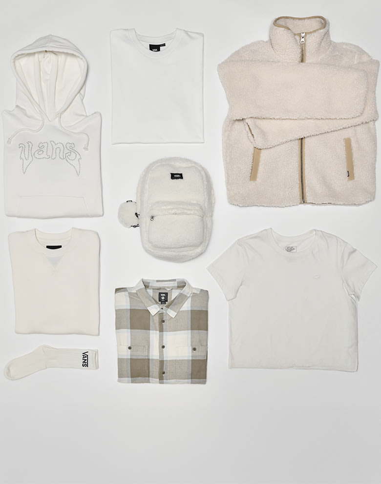 A group of white and light colored clothes and accessories are carefully placed on the floor of a grey photography studio.