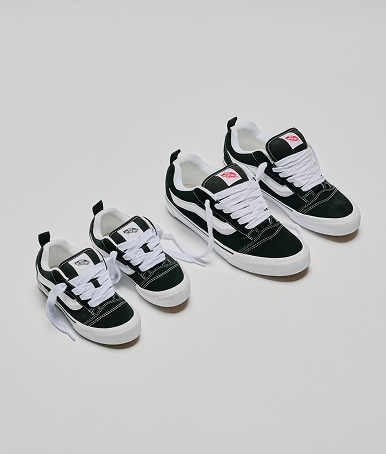 Two pairs of shoes on the floor. One is the Big Kids Knu Skool Shoe in black / white, the other is the Little Kids Knu Skool Shoe in black / white.