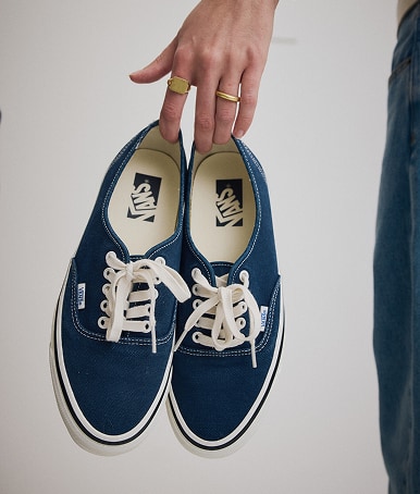 Close up of a woman holding a pair of the Premium Authentic Shoe in DUCK CANVAS Parisian Night by her index and middle finger.