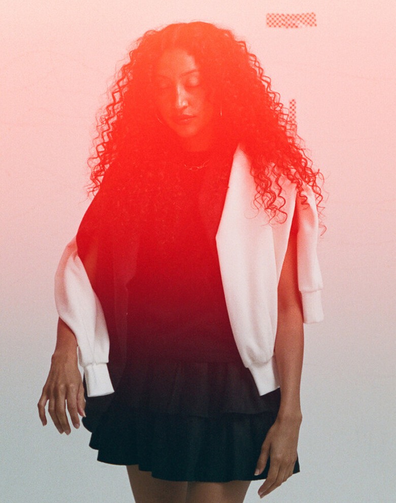 Woman in a photography studio with an orange and red gradient covering her. A sweatshirt is draped around her shoulders.