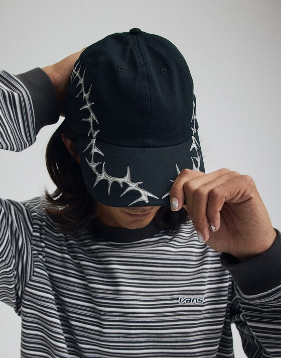 Image of a person wearing a Thorn Jockey Hat and a Wesley Stripe Long Sleeve Knit Shirt in a grey photography studio.