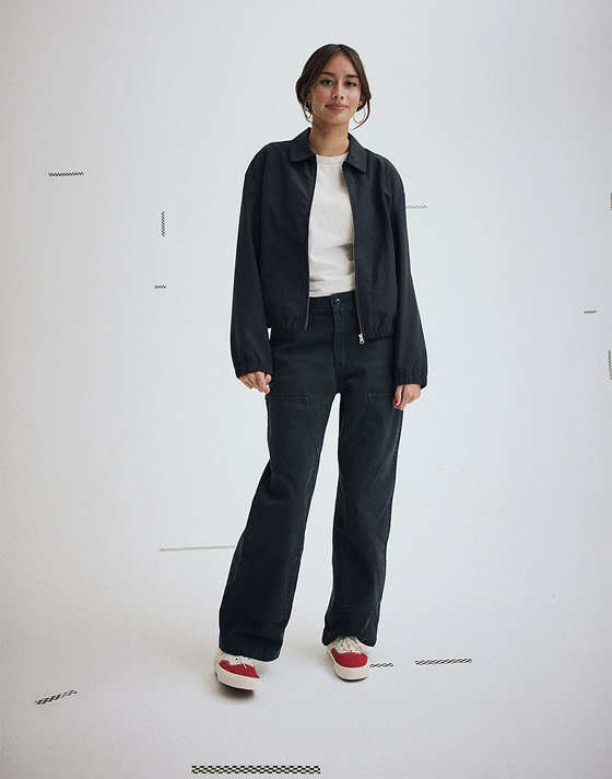 Wide shot of a woman wearing a Black Lightweight Bomber Jacket with Black Emily Carpenter Pants on.
