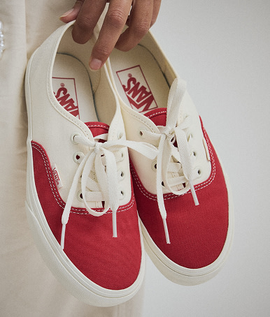 Close up of the Authentic Shoe in Racing Red. Someone is holding them and the shoes are hanging by their index and ring finger.