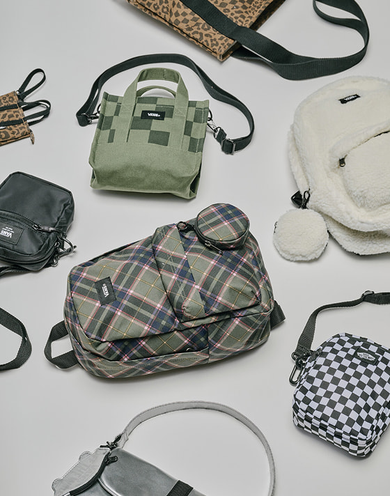 Wide shot of totes, bags, and backpacks on the ground of a grey photography studio.