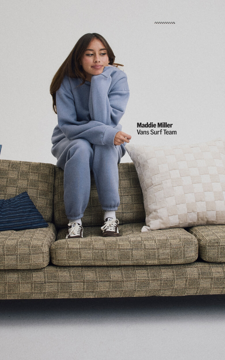 Maddie Miller of the Vans Surf Team laying down on a couch in a matching crewneck and sweatpants with a pair of Demitasse Brown Super Lowpro shoes on the floor.