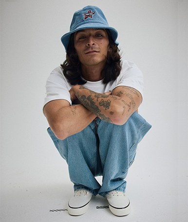 Person squatting in a grey photography studio wearing a Vans Denim Bucket Hat.