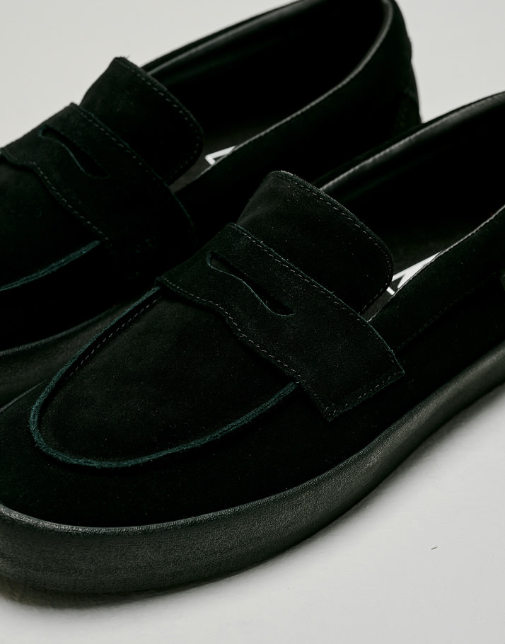 Close up of The Skate Loafer in Suede Black / Black on the floor of a grey photography studio.