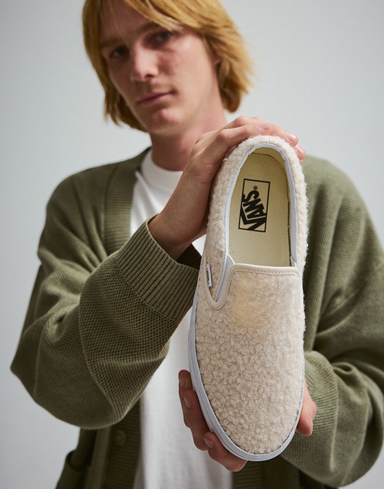 Close up of a man holding up a single Classic Slip-On Shoe in Marshmallow White.