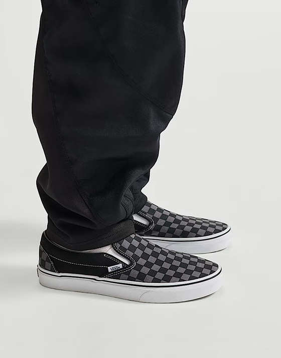 Medium shot from the knee down of someone wearing a pair of the Classic Slip-On Checkerboard Shoe in Checkerboard Black / Pewter Grey.