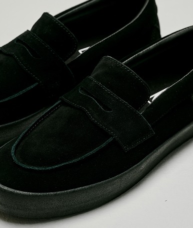 Close up of The Skate Loafer in Suede Black / Black on the floor of a grey photography studio.