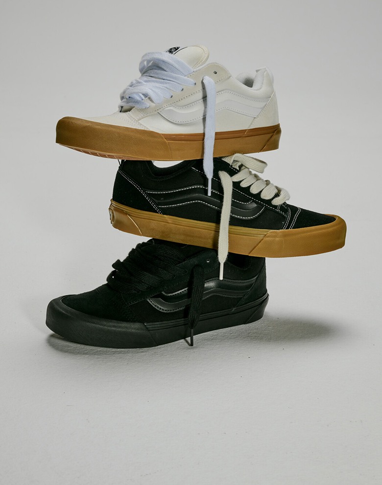 A Blanc De Blanc White Knu Skool shoe, a black gum Knu Skool shoe, and a black Knu Skool shoe stacked on top of each other in a photography studio.