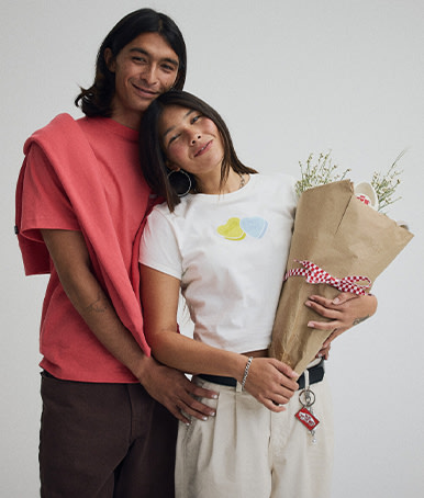 A young man embraces a young woman holding flowers wearing t-shirts from the Vans Valentine’s Day Collection.