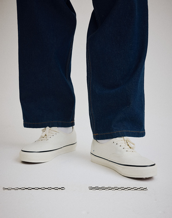 A knee-down shot of someone wearing the marshmallow white Premium Authentic with black pants in a photography studio.