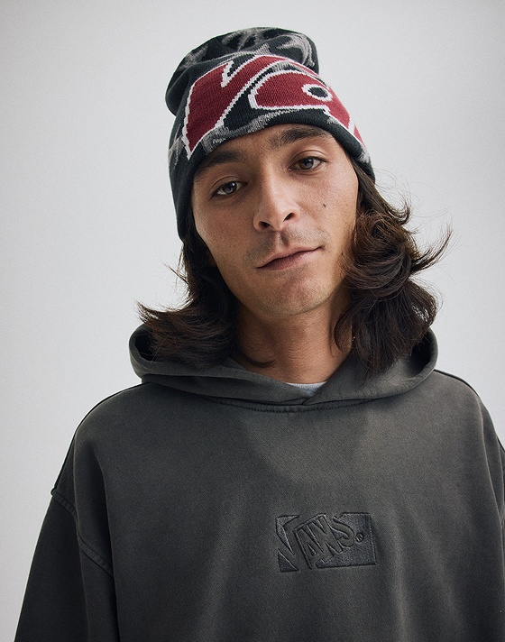 Medium shot of a man wearing the Vans Skull Beanie in Faded Black with the Premium Pullover Hoodie in Faded Black in a grey photography studio.