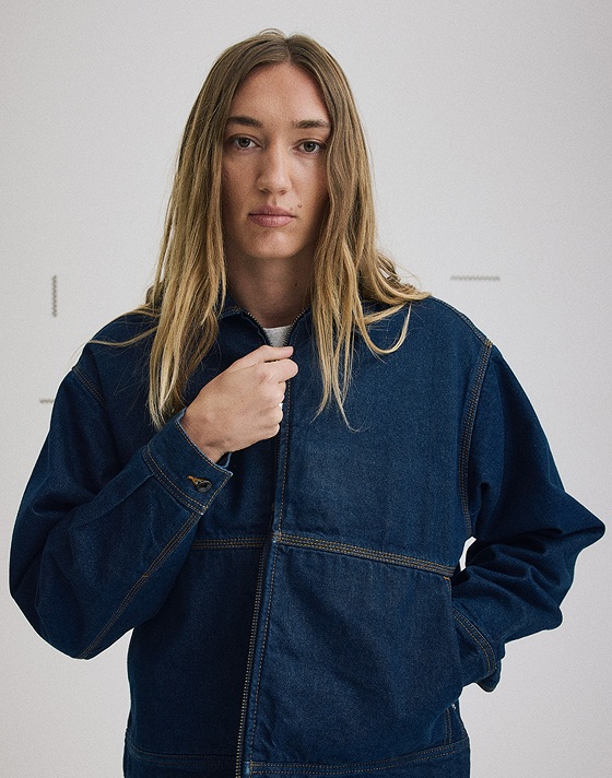 Medium shot of a woman wearing the Premium Denim Station Jacket in Dark Indigo Blue in a grey photography studio.
