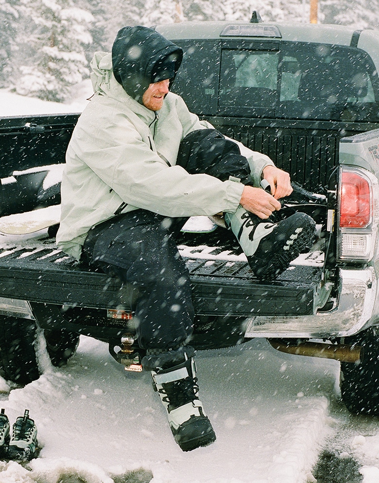 Image of a man on the tailgate of a truck lacing up a pair of the Infuse Snowboard Boot in Olive Grey while it's snowing.
