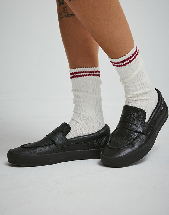 A knee-down shot of someone wearing the black Skate Loafer with white Vans crew socks and shorts in a photography studio.