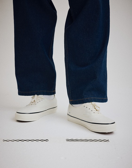 Knee down shot in a grey photography studio of someone wearing jeans with a pair of the Premium Authentic Shoe in Marshmallow White on.