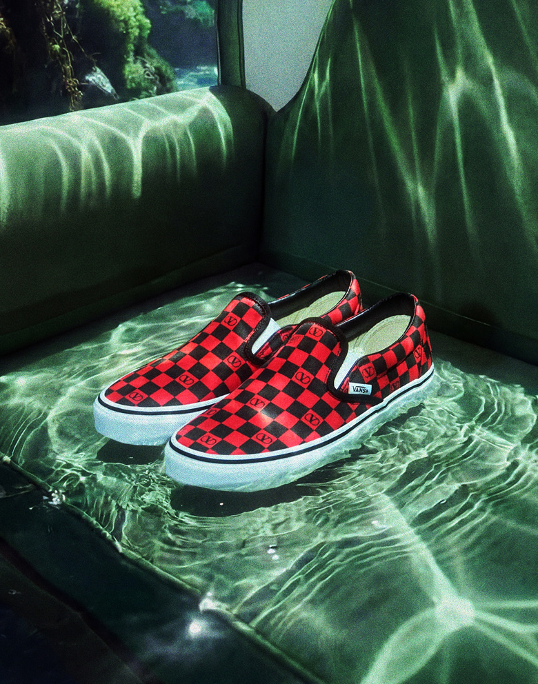 Medium shot of a pair of the Classic Slip-On Valentino Shoe sitting on a green couch under water with the ocean floor and a reef in the background.