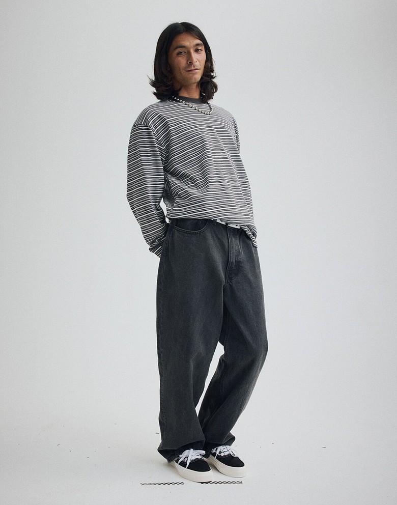 A young man poses in a photography studio wearing a faded black Wesley Stripe Long Sleeve Knit Shirt and Premium Old Skool Checkerboard shoes.