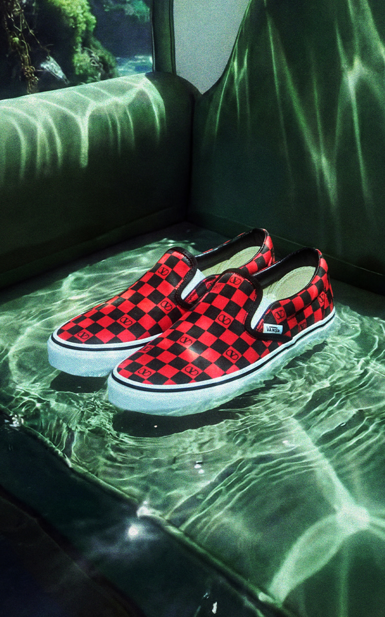 A red and black Checkerboard Classic Slip-On from the Valentino Garavani and Vans collection on a green felt sofa underwater in a reef.