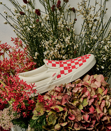 Red and white Classic Checkerboard Slip-On resting on a bed of flowers from the Vans Valentine’s Day Collection.
