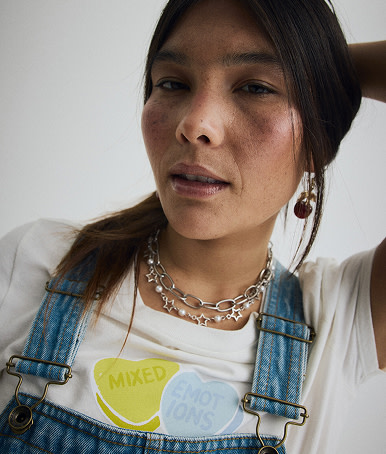 Close-up on a young woman wearing a Mixed Emotions t-shirt from the Vans Valentine’s Day Collection and blue Sirelle Overalls.