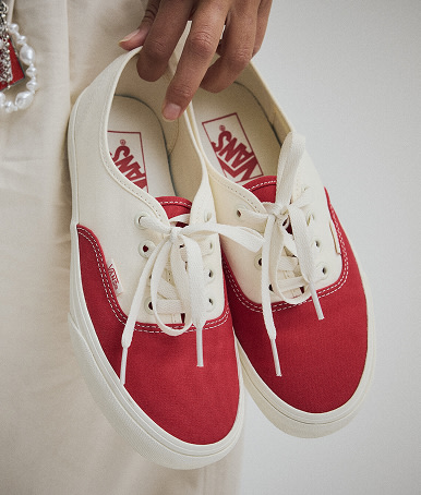 A pair of red and white Authentic shoe with its laces tied to a beige Old Skool shoe on the floor from the Vans Valentine’s Day Collection.