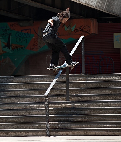 Wide shot of a skate boarder in the middle of grinding a rail down a cement staircase outside.