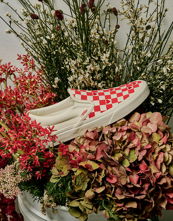 Medium shot of a pair of the Valentine's Classic Slip-On Checkerboard Shoe in Checkerboard Racing Red sitting in the middle of a bouquet.