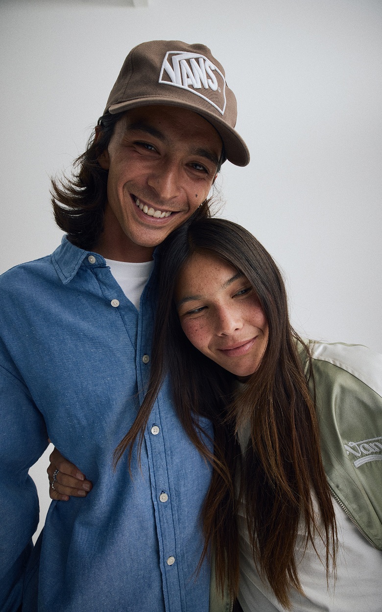 A young man and woman embrace each other in a photography studio in new Vans shirts, jackets, and hats.