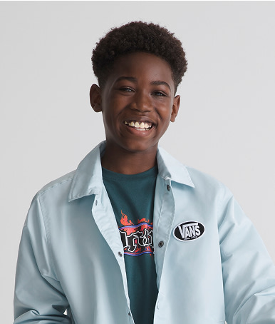 A young boy smiles in a photography studio wearing a mossy green olive Kids Night Spark T-Shirt and a denim overshirt.