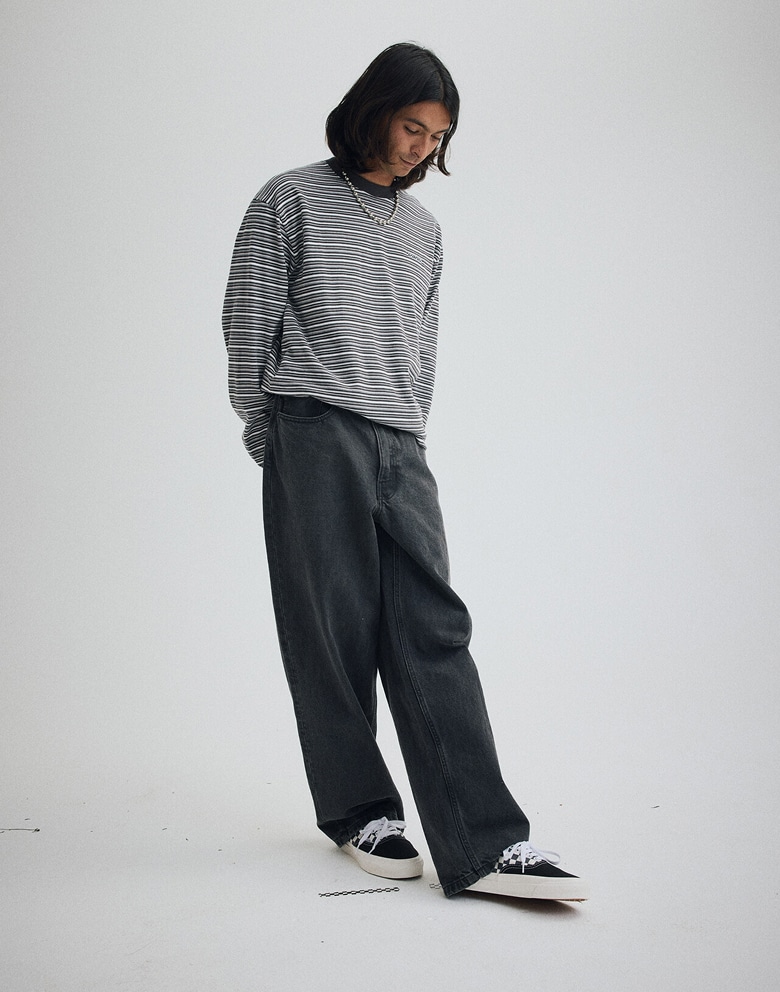 A young man poses in a photography studio wearing a faded black Wesley Stripe Long Sleeve Knit Shirt and Premium Old Skool Checkerboard shoes.