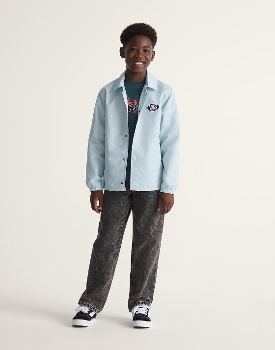 Full body shot of a kid wearing a Dawn Mist Blue Kids Torrey Coaches Jacket with black jeans and black and true white Little Kids Knu Skool Shoes.
