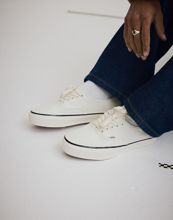 Medium shot knee down of someone sitting on the floor of a grey photography studio wearing the Marshmallow White Premium Authentic Shoe.