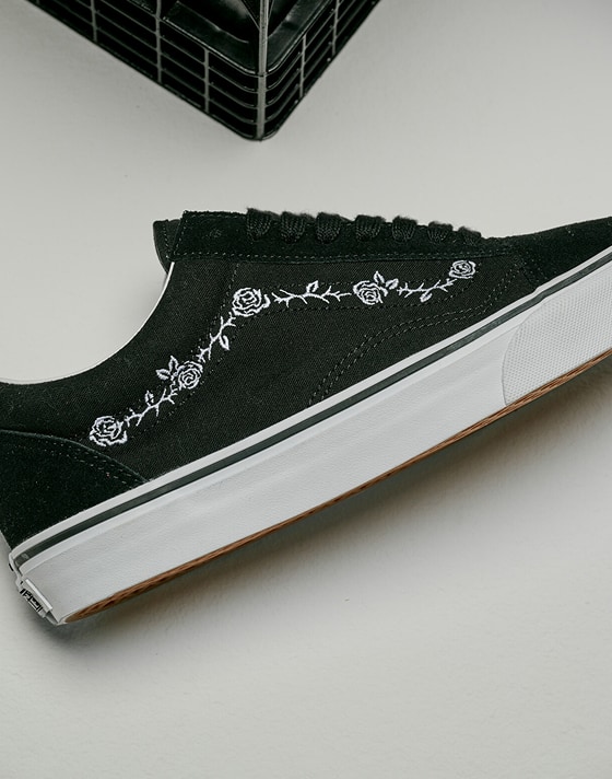 Close up of the Black and White Old Skool Shoe with an embroidered design of thorns and roses laying the floor of a grey photography studio.
