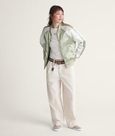 A young woman poses in a photography studio wearing a soft sage green Souvenir Jacket and Premium Authentic.