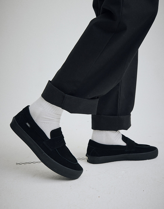 Close-up of a man wearing black suede Skate Loafers and white Vans crew socks.
