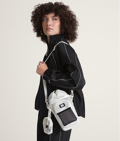 A young woman poses in a photography studio wearing a black Nyla tracksuit and a clear Junipero Water Bottle Bag.