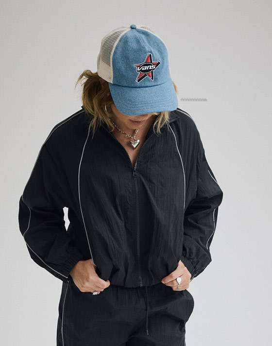 Vans Surf Team Rider Karina Rozunko poses in a photography studio wearing a black Nyla tracksuit.