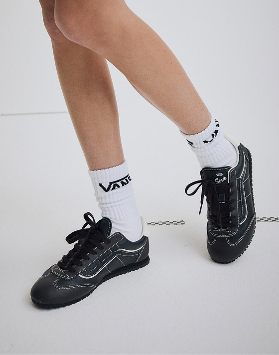 Close-up on a woman wearing black leather Super Lowpro with white Vans Crew socks.