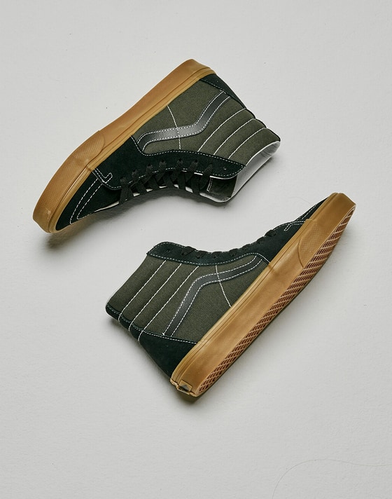Medium shot of a pair of the Gum Obsidian Fern Green Sk8-Hi laying on the floor of a grey photography studio.