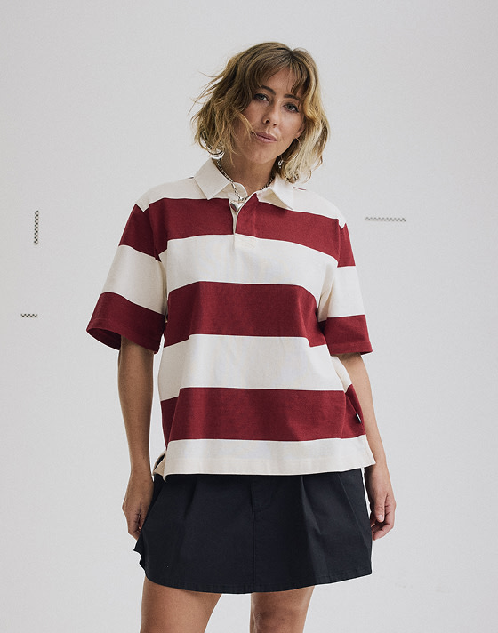 Vans Surf Team Rider Karina Rozunko poses in a photography studio wearing a bordeaux red and white striped SS Rugby polo.