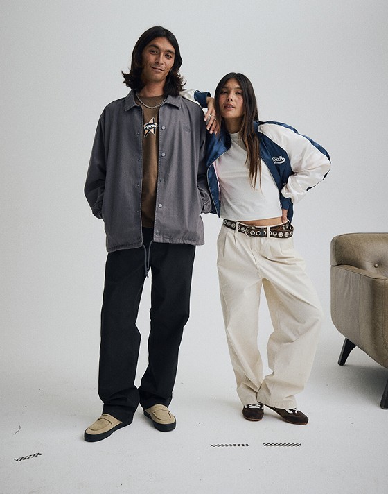 A young man and young woman pose together in a photography studio wearing tan Skate Loafers and black Super Lowpro.