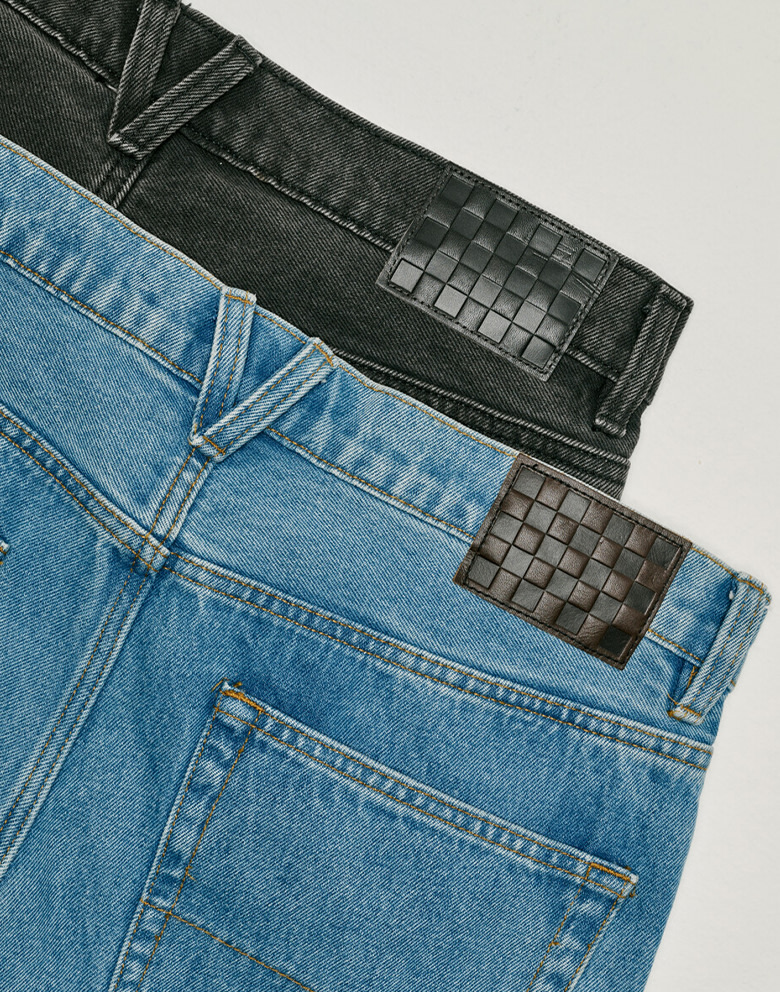 Two pairs of Check-5 Loose Denim Pants on the floor of a photography studio, one blue and one black.